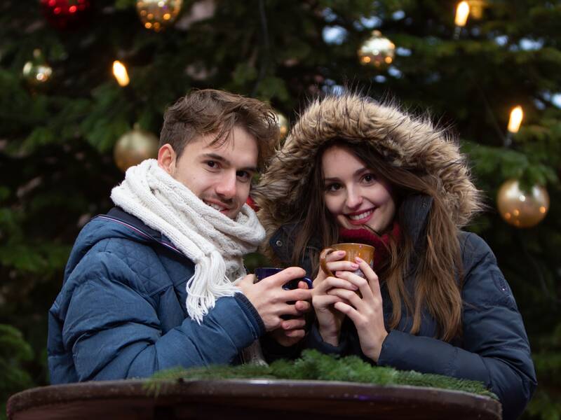 Ein Mann und eine Frau mit Tassen in der Hand vor einem Weihnachtsbaum