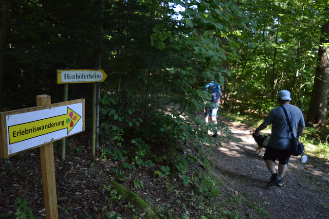 Schild im Vordergrund und Menschen mit Hund im Hintergrund