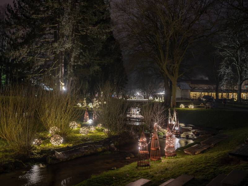 Das Bild zeigt den nächtlichen Kurpark, der von Lichtelementen punktuell erleuchtet ist. Die Lichtelemente sind an den Ufern eines kleinen Flusses aufgebaut, der durch den Kurpark fliesst.