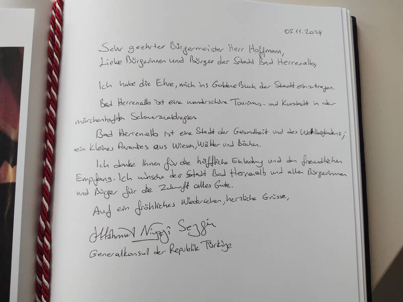 Im Bild zu sehen ist das aufgeschlagene Goldene Buch der Stadt Bad Herrenalb mit dem handschriftlichen Eintrag des türkischen Generalkonsuls Mahmut Niyazi Sezgin. In seinem Eintrag betonte Generalkonsul Sezgin die Schönheit Bad Herrenalbs als „Paradies aus Wiesen, Wäldern und Bächen“ und wünschte „allen Bürgerinnen und Bürgern für die Zukunft alles Gute.“