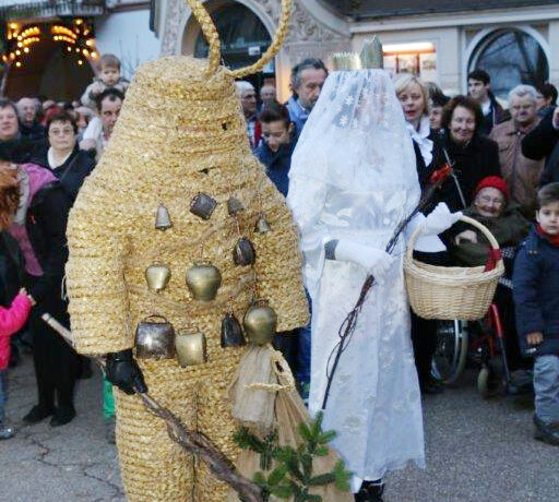 Zwei Personen, verkleidet in auffälligen, traditionellen Kostümen als Christkind und Pelzmärtle, sind umgeben von einer Menschenmenge,