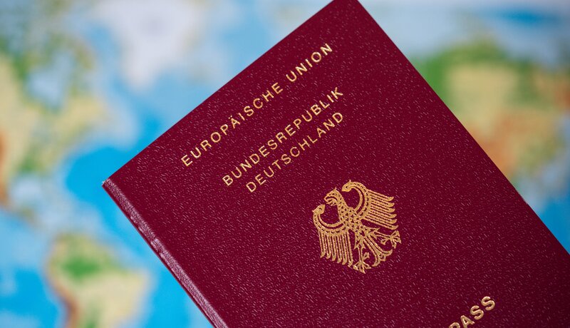 Ein deutscher Reisepass liegt vor einem unscharfen Hintergrund, der eine Weltkarte zeigt.