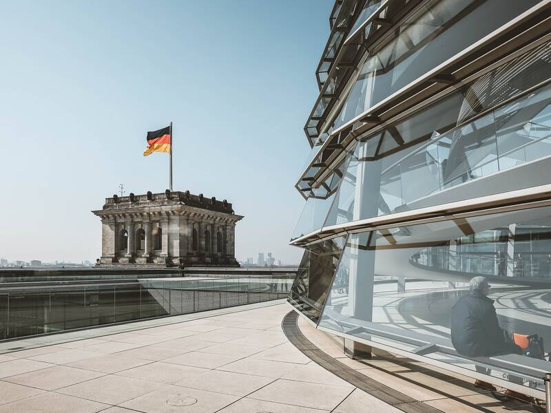 Ein Mann sitzt in der gläsernen Kuppel des Reichstagsgebäudes in Berlin, während im Hintergrund die deutsche Flagge flattert.